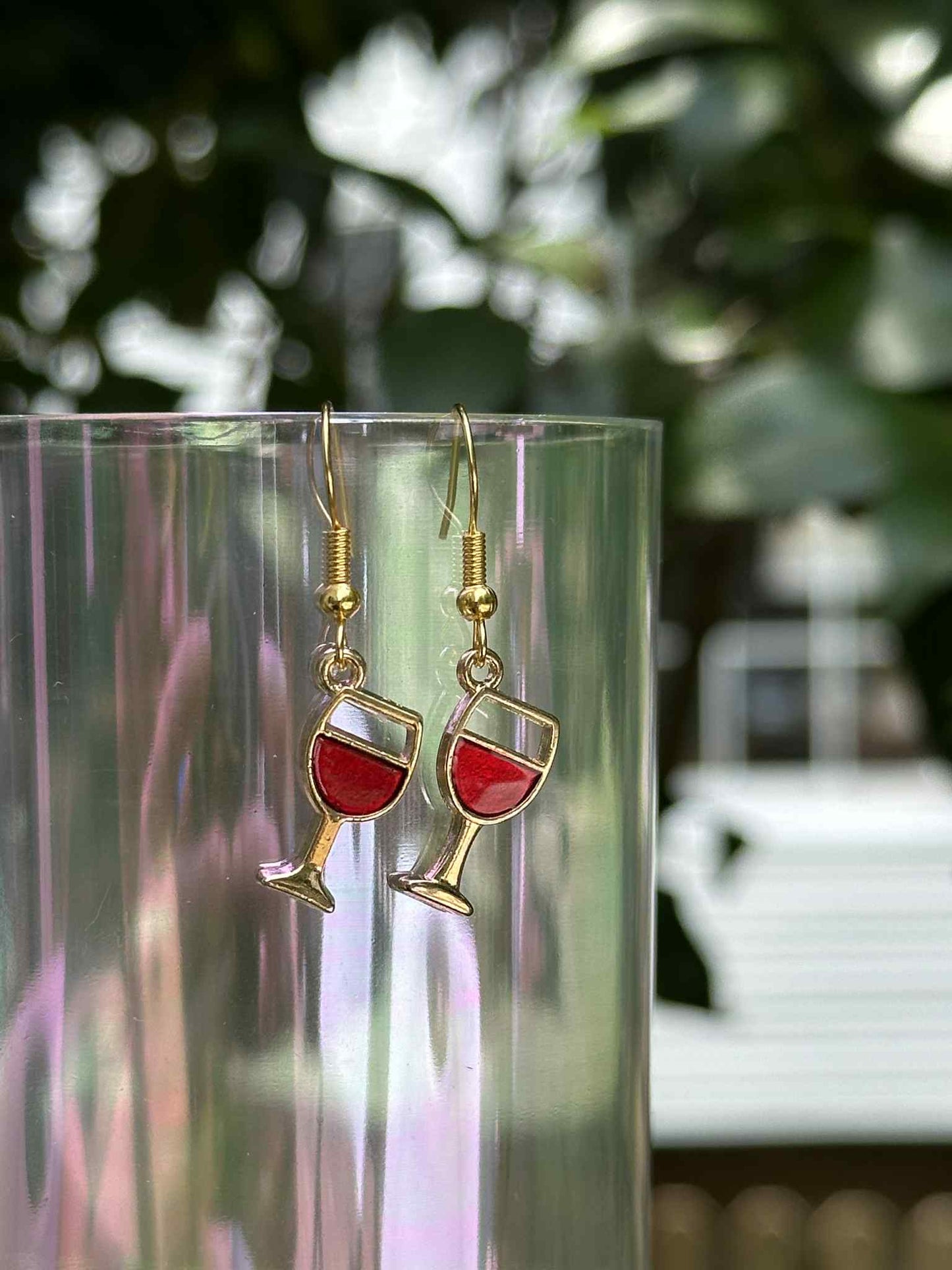 Wine glass earrings with red liquid design on a clear stand with a blurred background