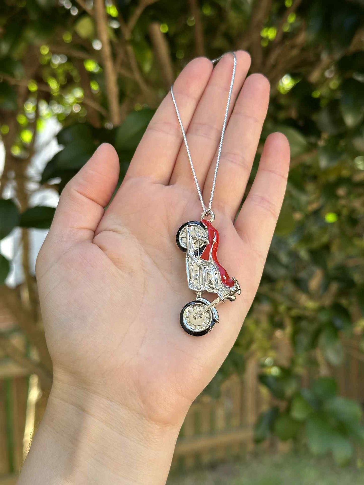 Hand holding a small decorative item on a chain with a blurred green background