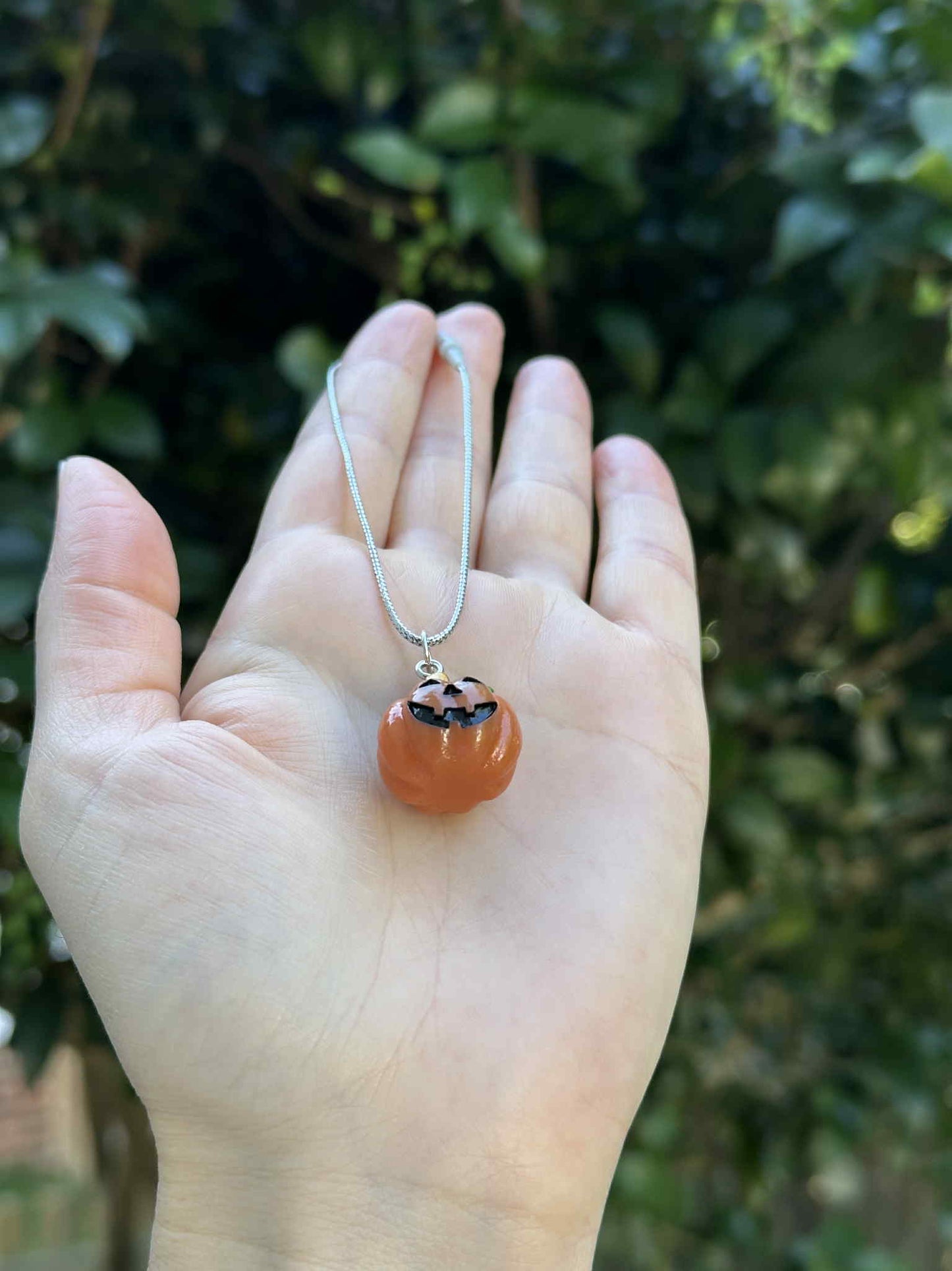Mini pumpkin jack-o’-lantern ornament with silver hanging cord, held in hand outdoors.