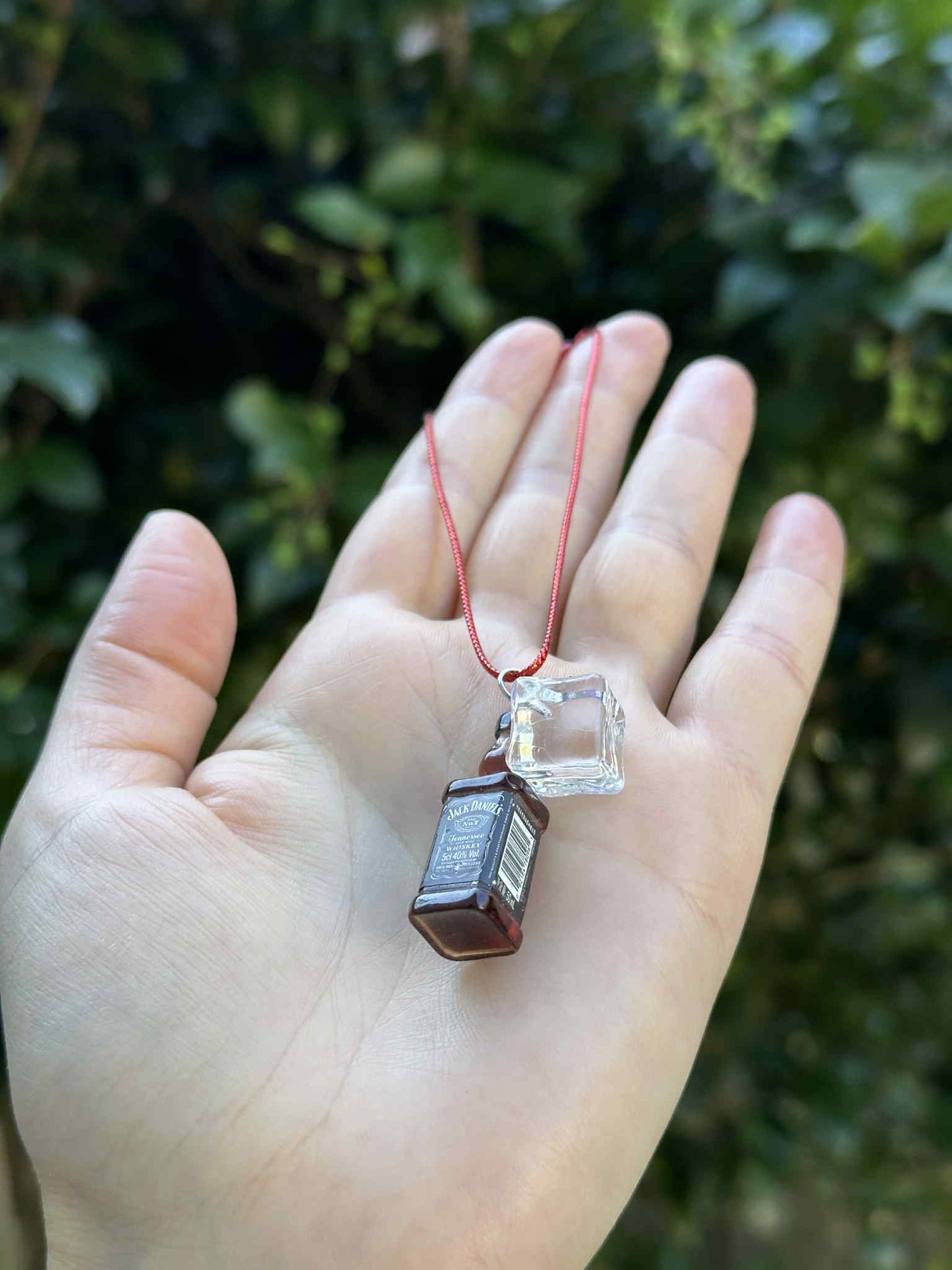 Miniature brown bottle and clear glass ornament with red hanging cord, held in hand outdoors.