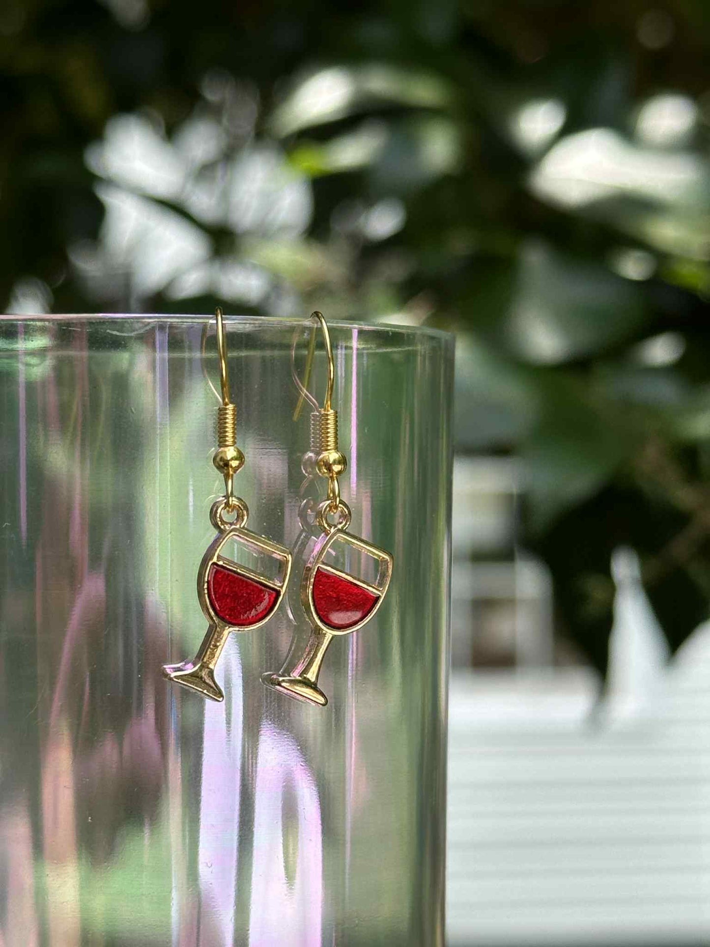 Wine glass earrings with red liquid design on a clear stand with a blurred green background