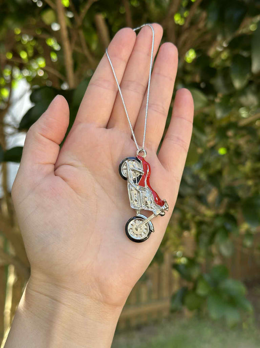 Hand holding a necklace with a stroller pendant against a blurred green background
