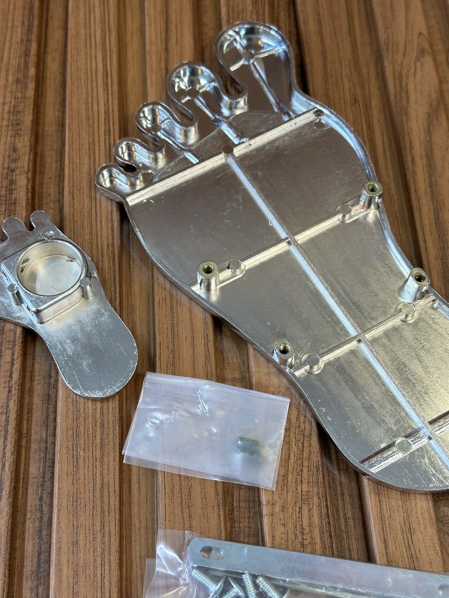 Metallic mechanical component on a wooden surface with screws and a plastic bag.
