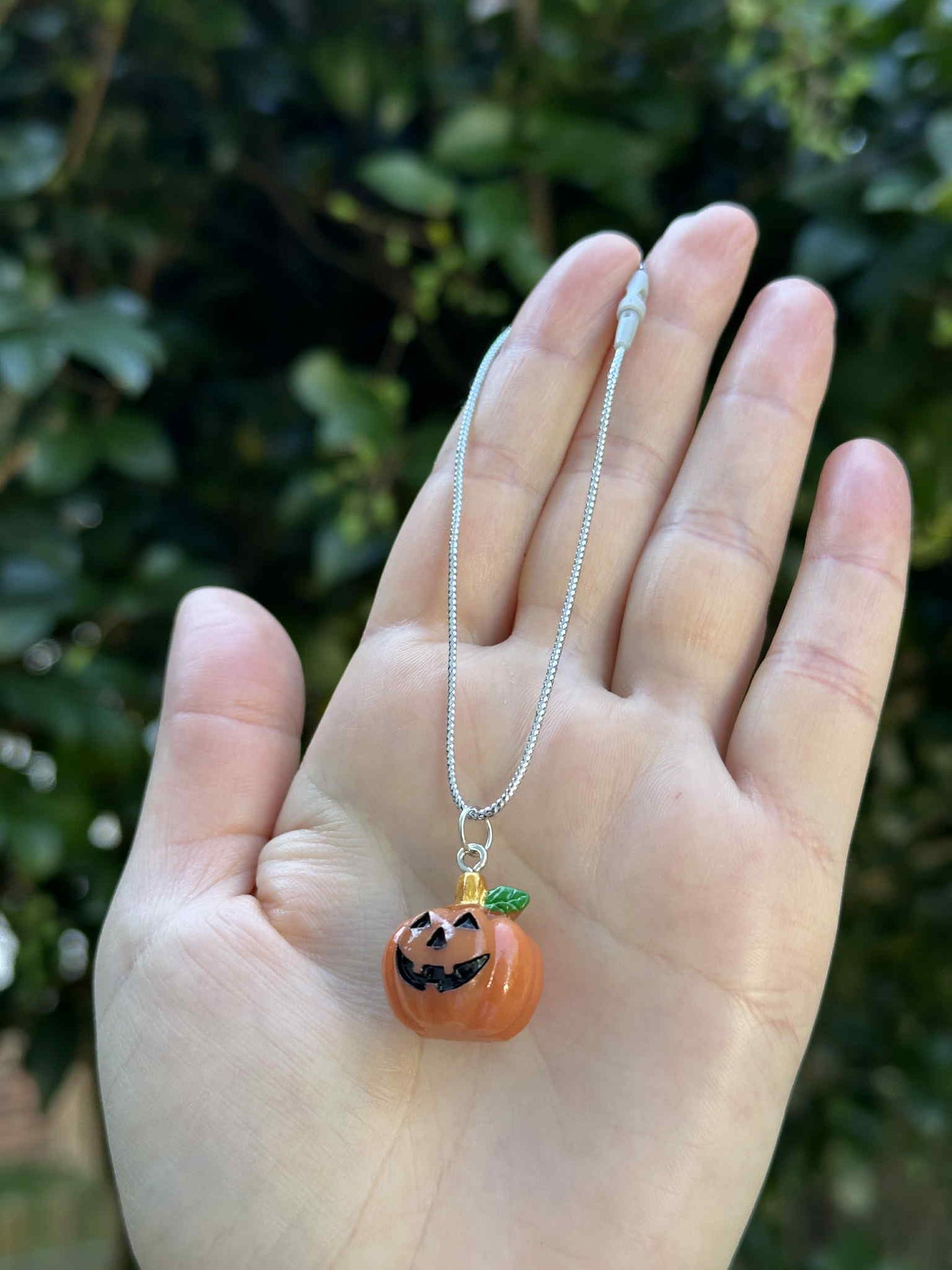Mini pumpkin jack-o’-lantern ornament with silver hanging cord, held in hand outdoors.