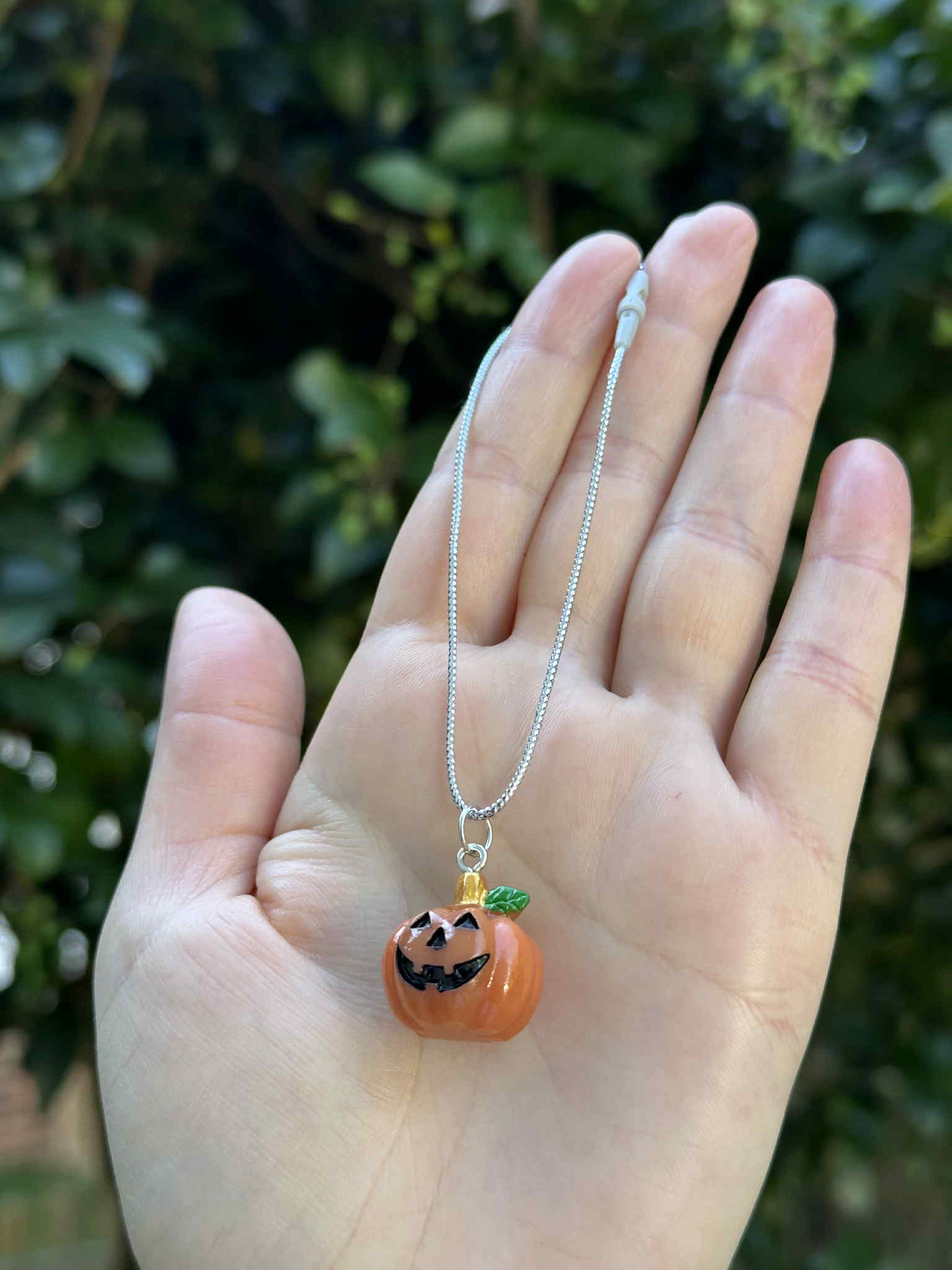 Mini pumpkin jack-o’-lantern ornament with silver hanging cord, held in hand outdoors.