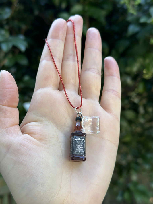 Miniature brown bottle and clear glass ornament with red hanging cord, held in hand outdoors.