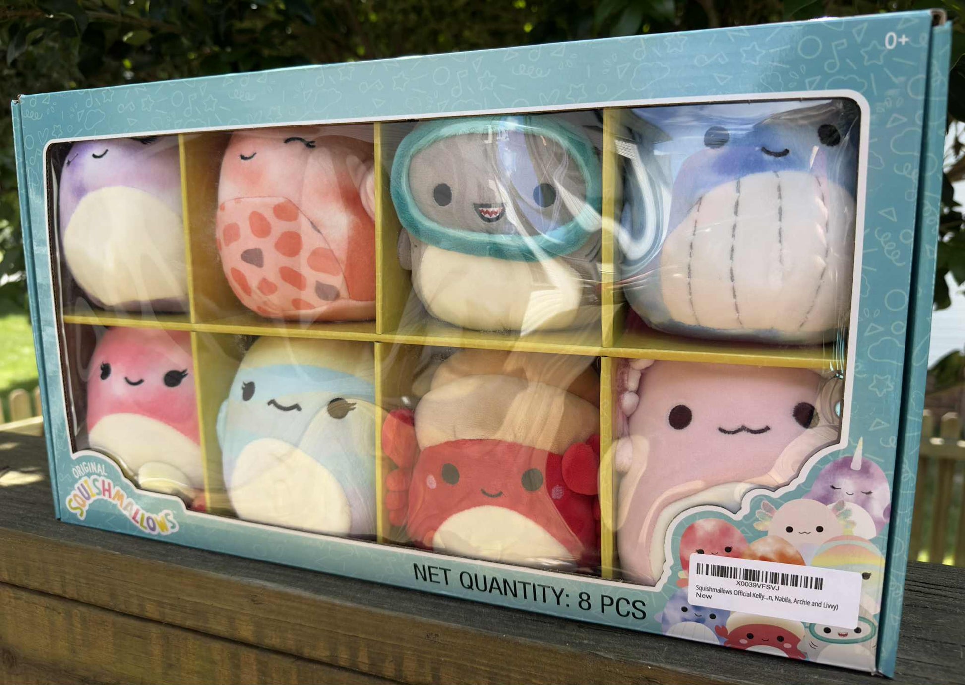 Box of eight cute plush toys with various designs on a wooden surface.