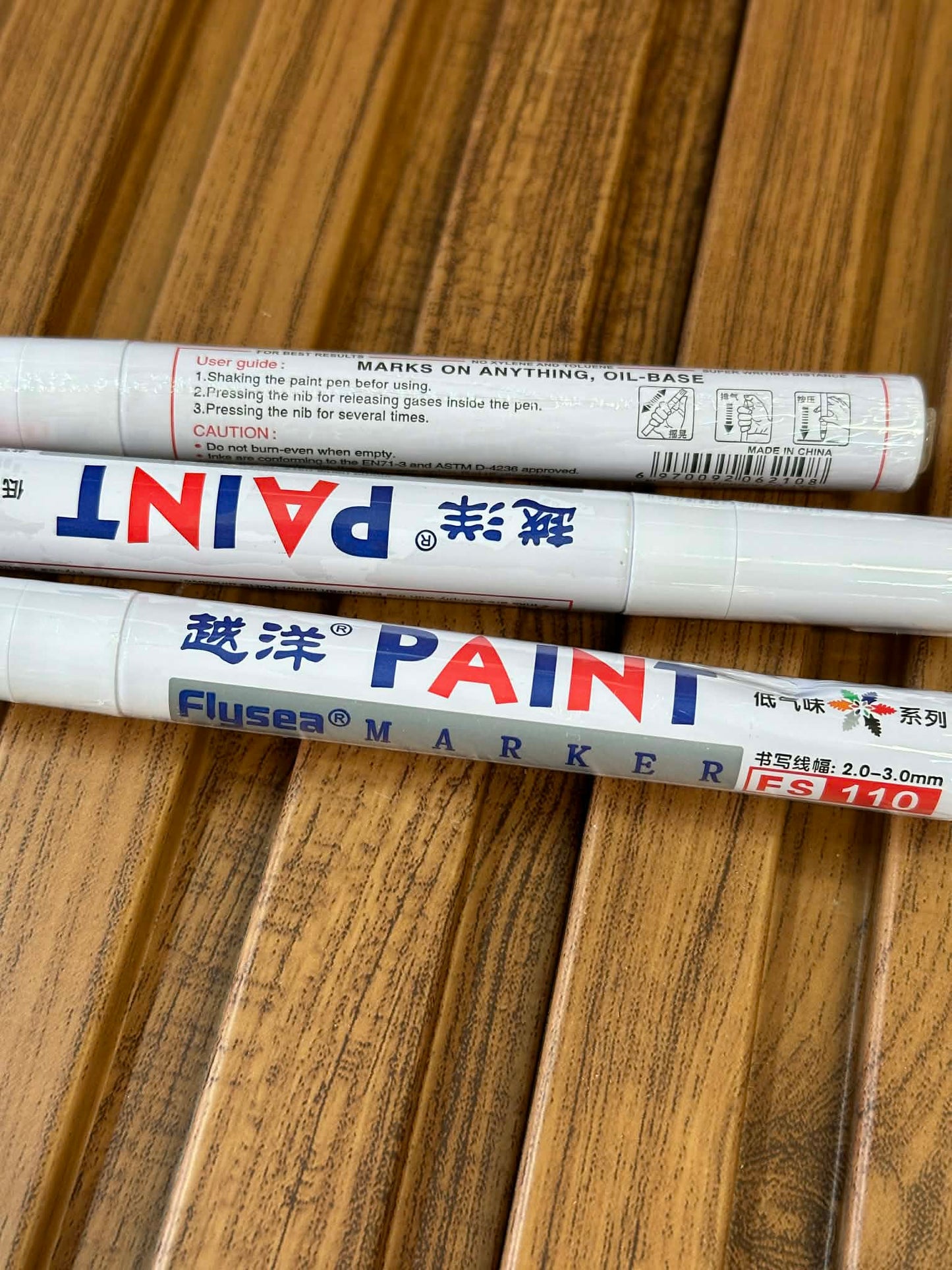 Three paint markers with visible brand names on a wooden surface