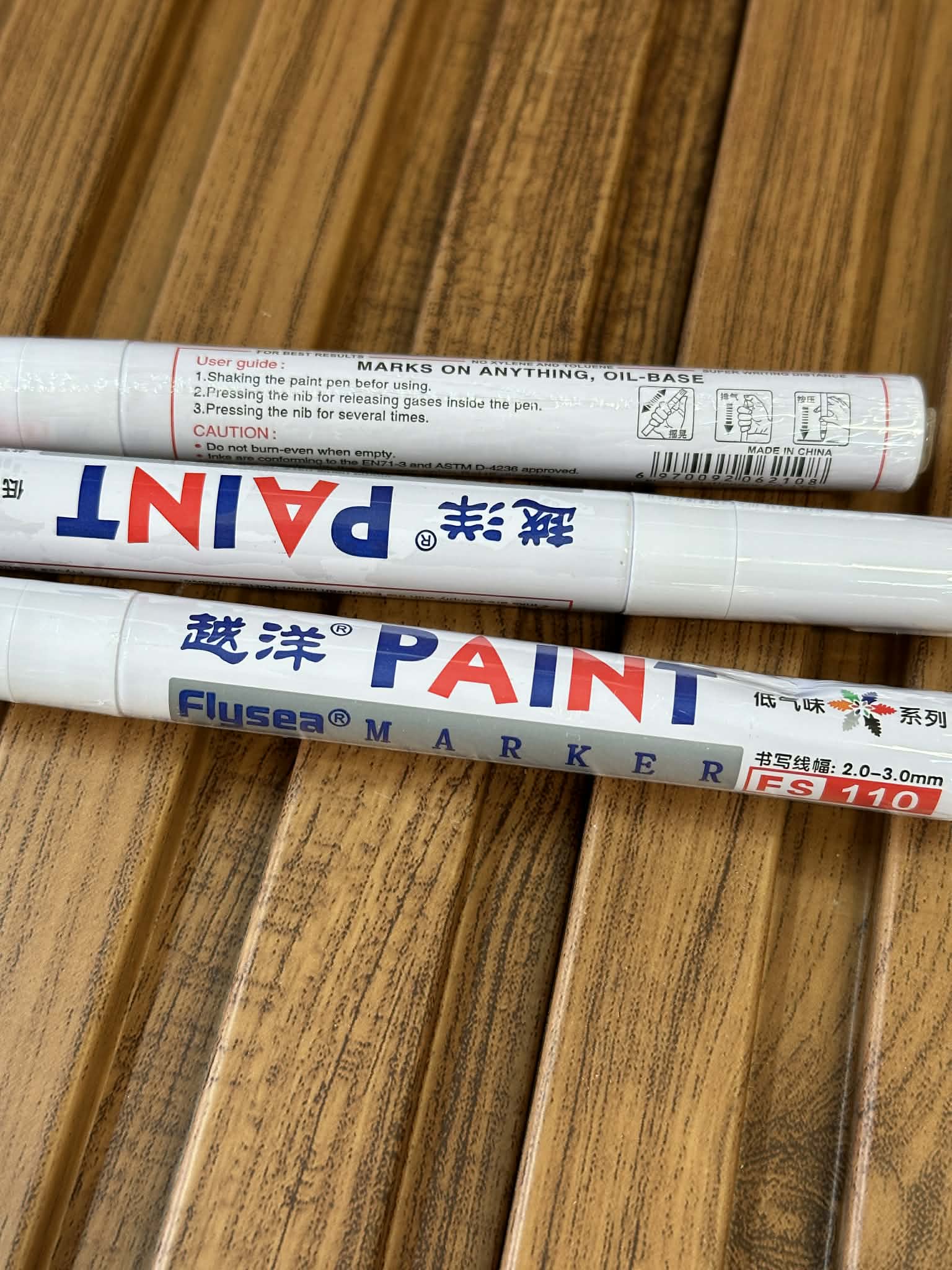 Three paint markers with visible brand names on a wooden surface