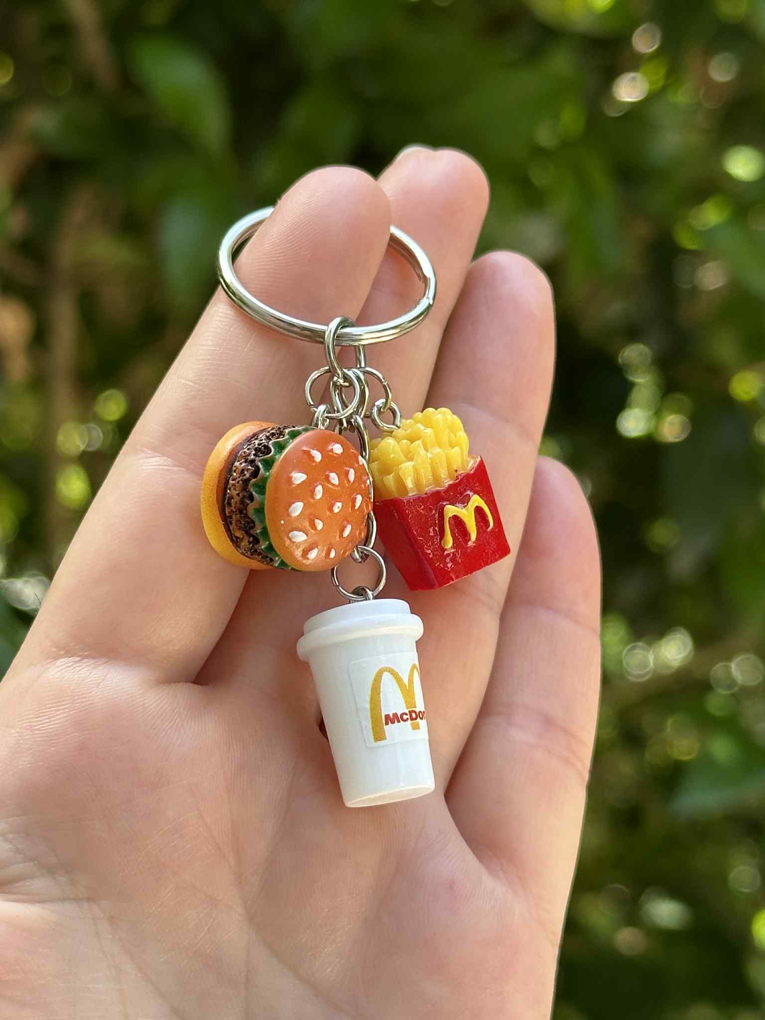 Keychain with McDonald's-themed charms including a burger, fries, and cup held in a hand with a blurred green background.