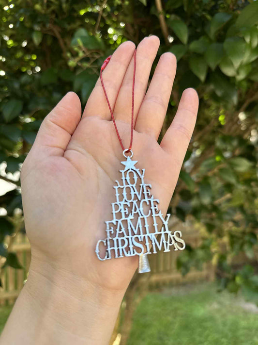 Hand holding a Christmas tree-shaped ornament with engraved text against a green outdoor background