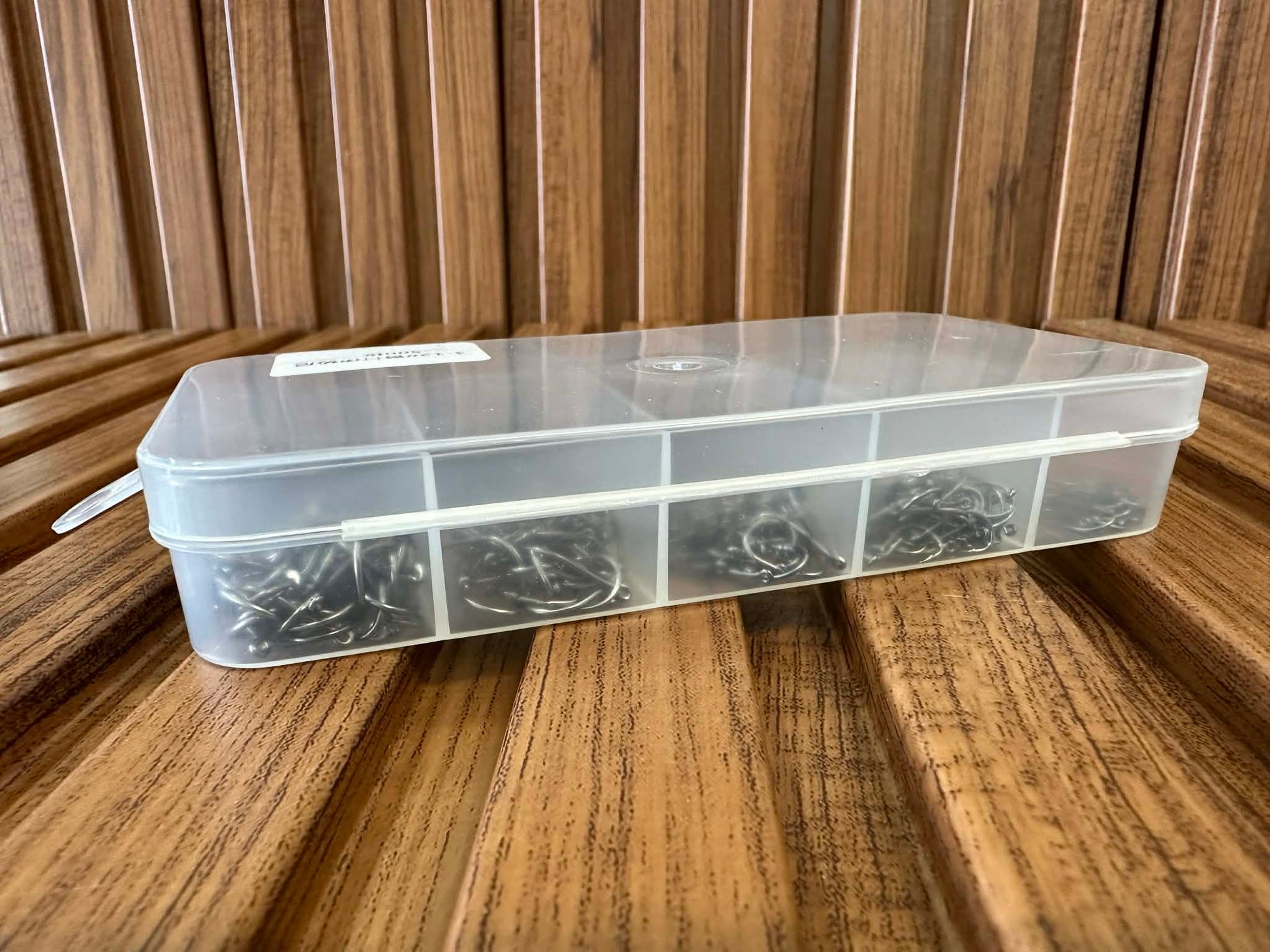 Clear plastic tackle box with compartments on a wooden surface