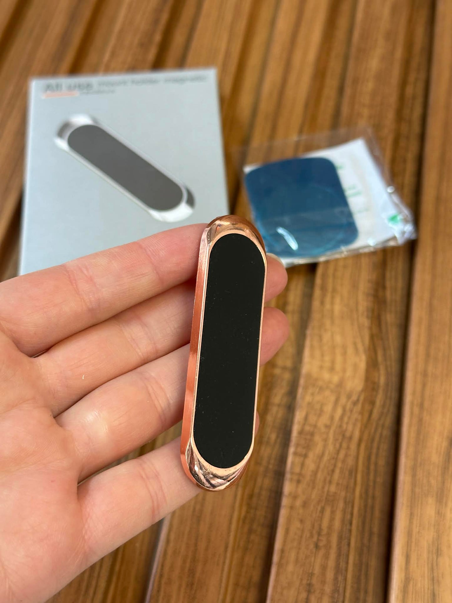 Rose gold and black device held in a hand with packaging in the background on a wooden surface