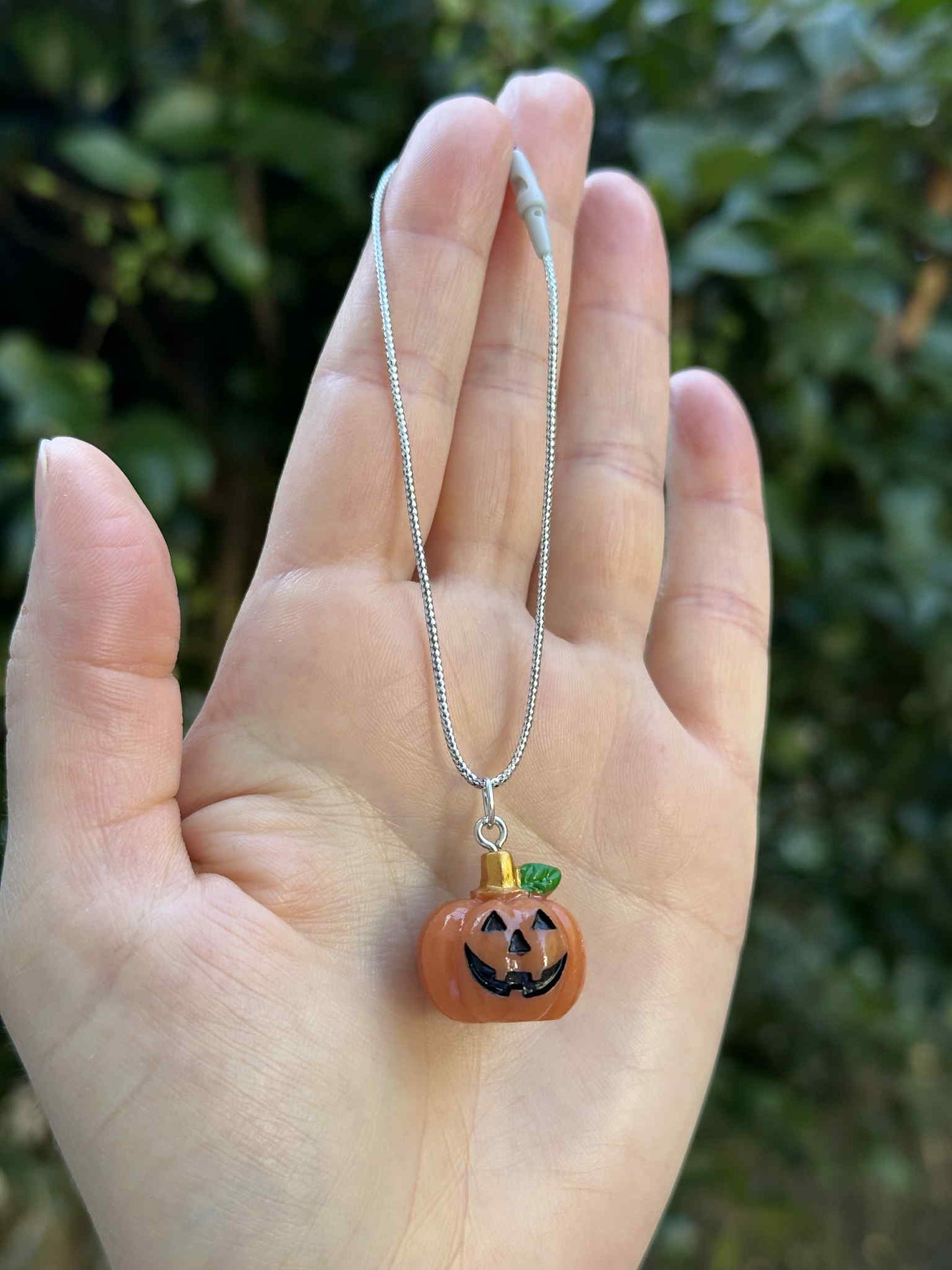 Mini pumpkin jack-o’-lantern ornament with silver hanging cord, held in hand outdoors.