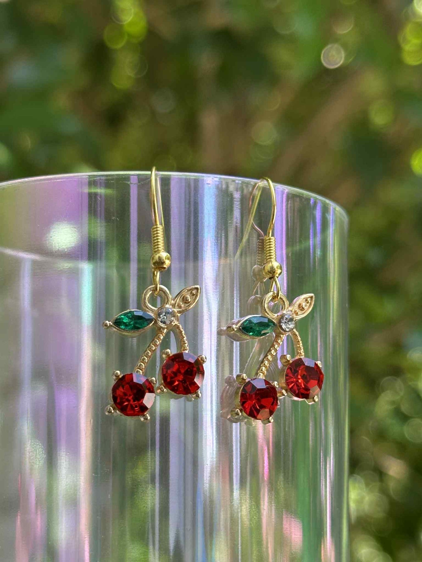 Gold earrings with red gemstones on a clear stand with a blurred green background
