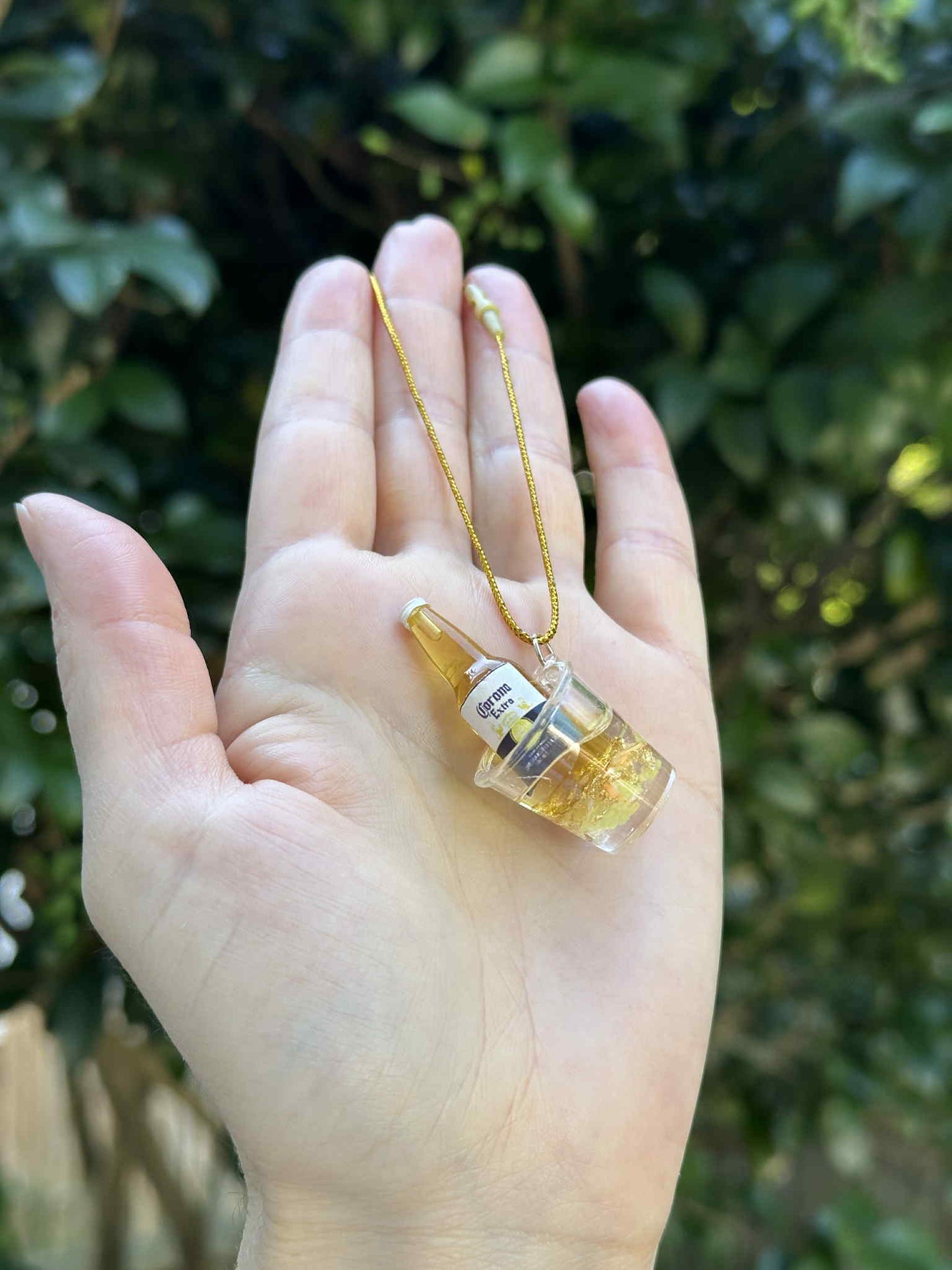 Miniature golden bottle in ice bucket ornament with gold hanging cord, held in hand outdoors.