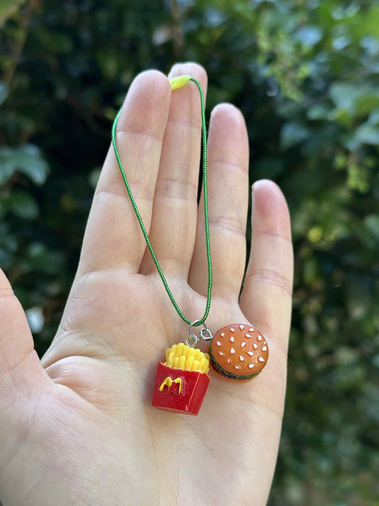 Mini burger and fries ornament with green hanging cord, held in hand outdoors.
