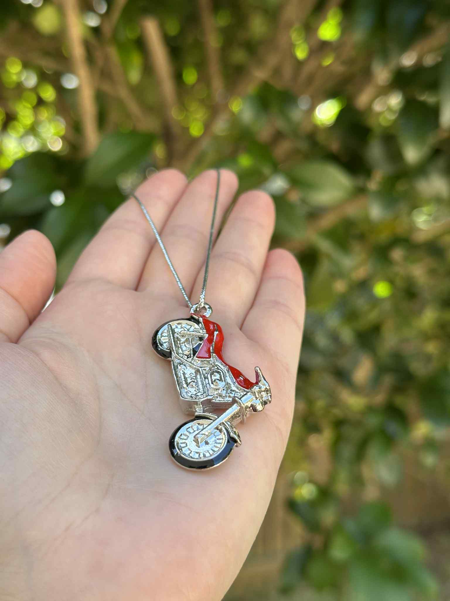 Hand holding a decorative keychain shaped like a baby stroller with a blurred green background