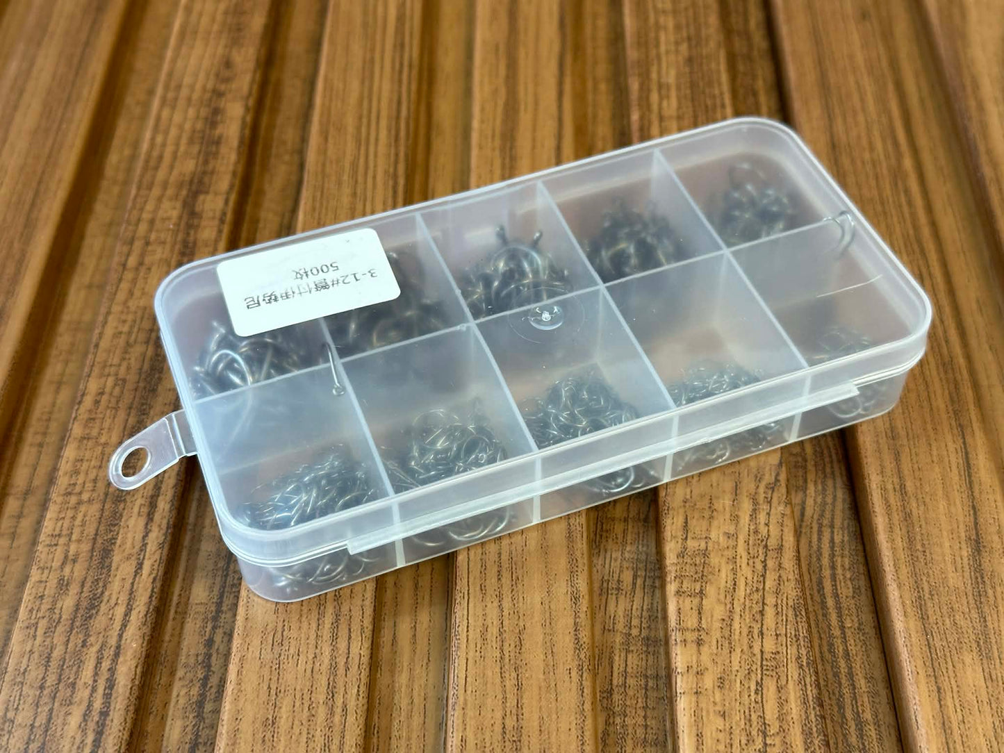 Clear plastic box with compartments containing small metal items on a wooden surface