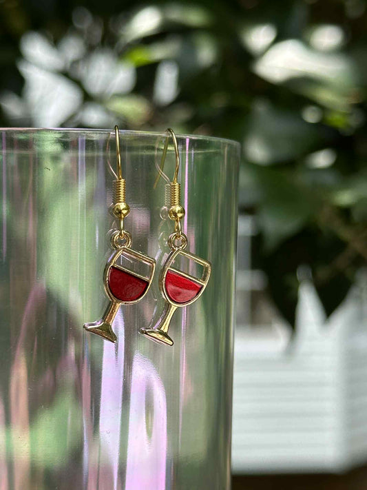 Wine glass earrings on a clear stand with a blurred green background