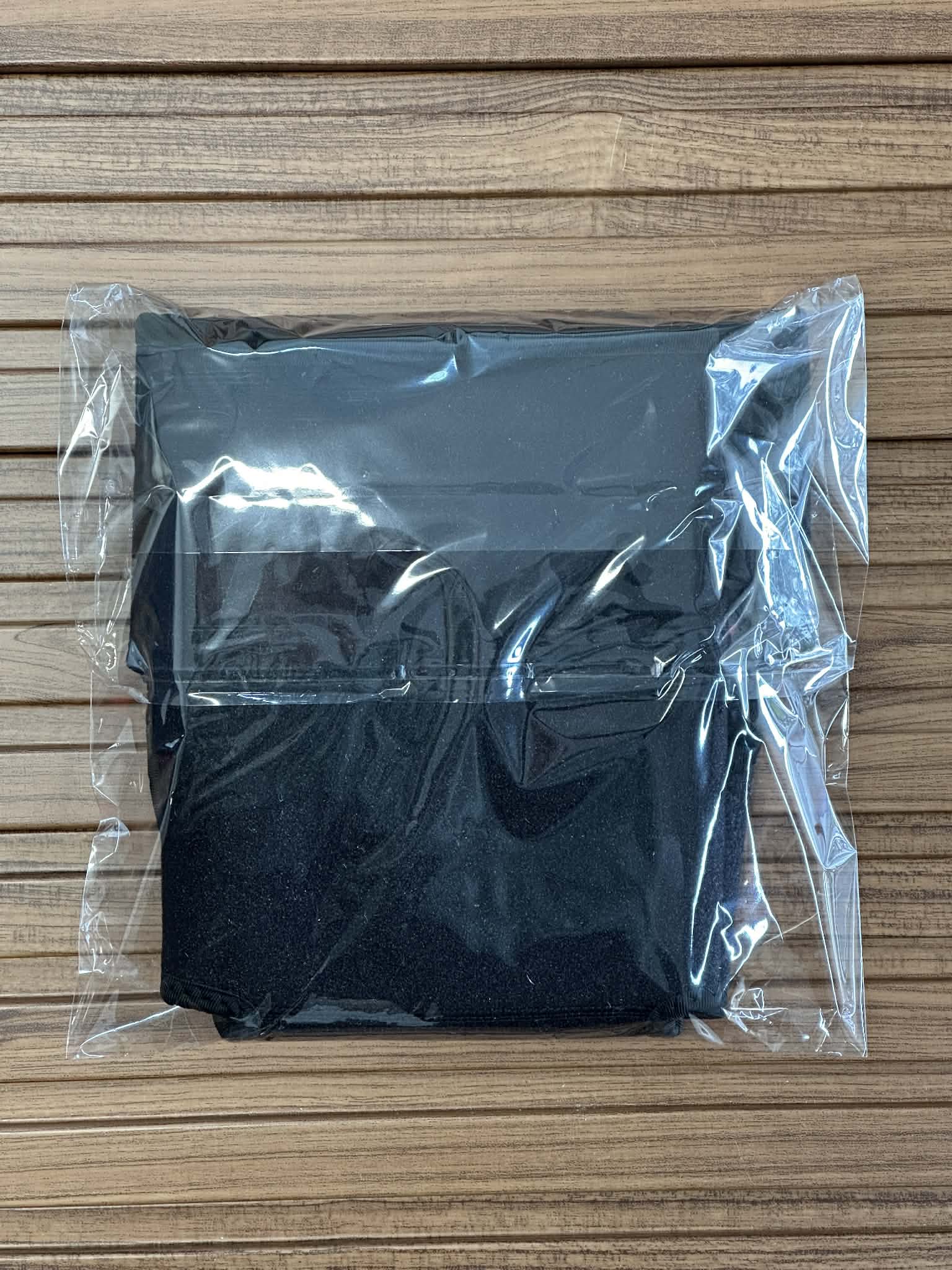Black item wrapped in clear plastic on a wooden surface